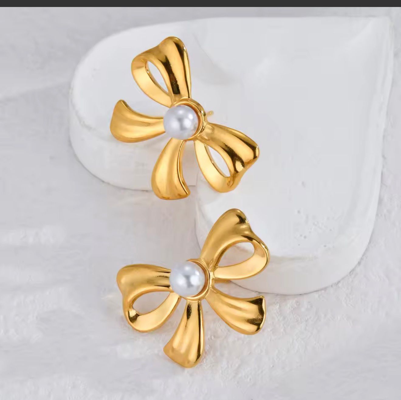 Gold Bow Pearl Stud Earrings on stone
