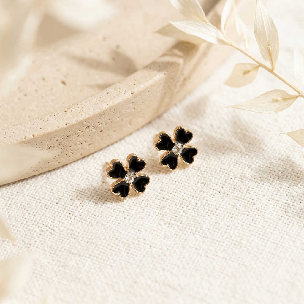 Black Clover Gold Stud Earrings laid flat on cream linen with dried botanicals